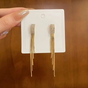 Detail of gold tassel earrings with rhinestones held against a dark wooden background