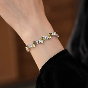 Close-up of silver bangle with intertwined green and white zircon stones on wrist