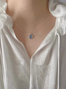 Detail of an oval light blue aquamarine pendant on a silver chain worn by a model