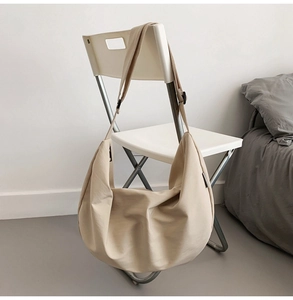 Detail of a large beige Oxford fabric hobo bag hanging on a chair in a minimalist setting