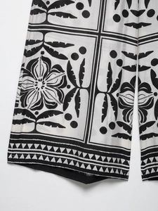 Détail d'un pantalon large avec imprimés floraux noirs et blancs et bordure géométrique
