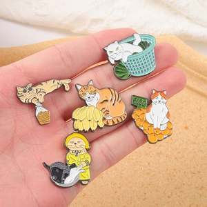 Set of five creative cat enamel pins held in hand to show the actual product size