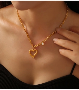 Détail du collier cœur évidé doré avec une perle blanche sur le cou d'un modèle