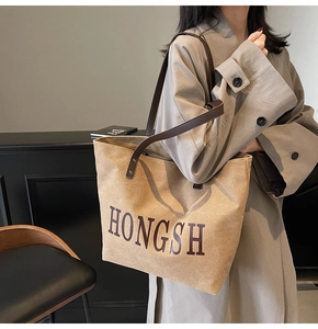 Detail of khaki canvas tote with brown leather straps worn with a trench coat