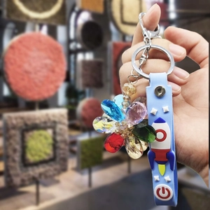 Colorful crystal flower keychain with blue rocket silicone wristband held in hand