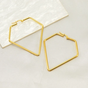 Modern gold irregular geometric hoop earrings on white marble textured coaster