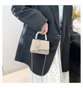 Detail of elegant apricot crossbody bag with pearl handle and glitter finish flap