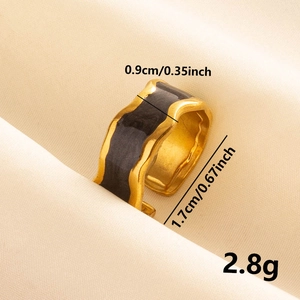 Irregular gold ring with black enamel wavy detail on beige fabric background