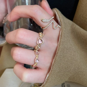Detailed view of a gold snake ring with pavé stones and a pink heart gem ring on a hand
