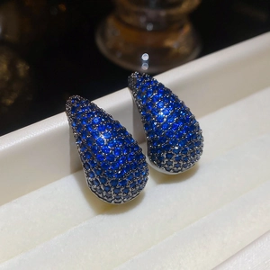Macro shot of silver drop earrings with pavé blue cubic zirconia in a white tray