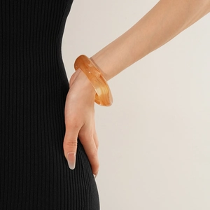 Detailed view of an amber resin cuff bracelet with marble texture worn by a model