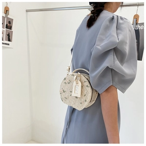 Detail showing round straw bag with floral embroidery and adjustable white strap