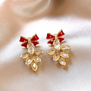 Détail de boucles d'oreilles nœud rouge avec finition dorée et cristaux en feuilles