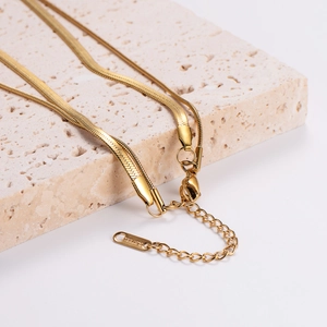 Double-layered gold stainless steel snake chain necklace displayed on a stone base