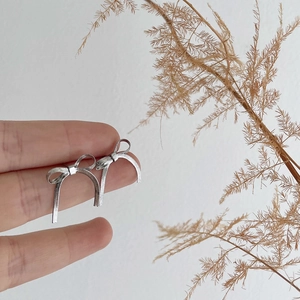 Detailed close-up of silver bow-shaped snake chain earrings held with a natural branch