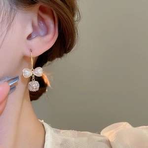 Detailed view of elegant gold bow earrings with pearls and zircon on a model
