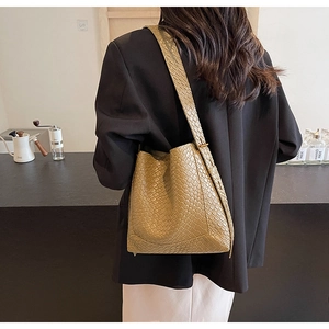 Detail of khaki woven texture handbag featuring a wide shoulder strap in a cafe setting