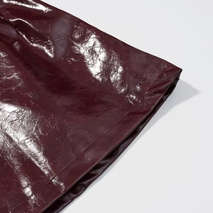 Dettaglio ravvicinato in pelle verniciata rosso vino lucido con trama stropicciata