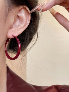 Close-up of model wearing large burgundy red enamel hoop earrings with silver needle