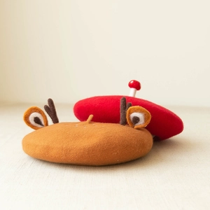 Flat lay of brown elk antler and red mushroom wool felt berets on a soft beige fabric background