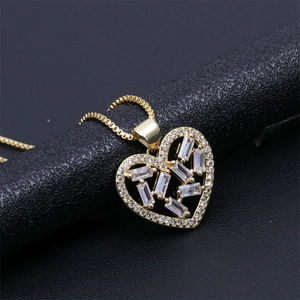 Detail of gold-plated heart pendant with zircon stones on a black textured stand