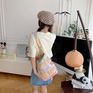 Detail view of colorful striped canvas crossbody bag worn by a model in a cozy room