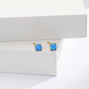 Close-up of blue opal stud earrings with gold four-claw setting on white decor blocks