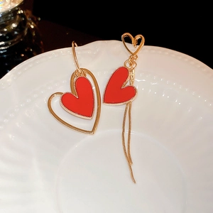 Detail view of gold asymmetrical heart earrings with red enamel and tassel chains