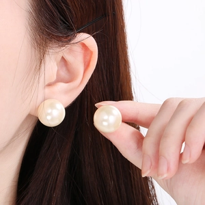Close-up of large round cream pearl stud earrings worn by model with glossy finish
