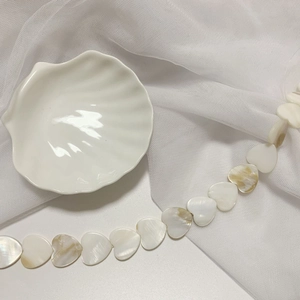 Detail view of heart-shaped natural shell beads with pearl luster on white tulle background