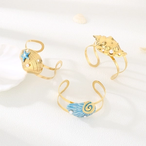 Ocean theme gold bracelets with sea shells, pearls and blue enamel on sand background