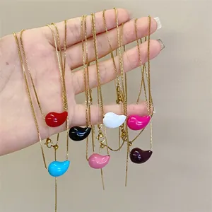 Detail of colorful enamel bean necklaces in gold finish held by hand to show textures