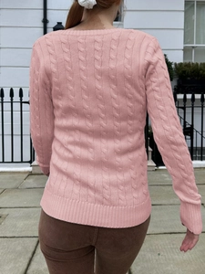 Back view of a pink cable-knit sweater with ribbed cuffs and hem against a white wall