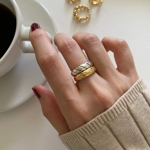 Detail of twisted croissant rings in gold and silver finish worn with coffee cup