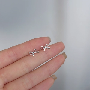 Detailed macro view of small silver bow stud earrings held on a finger for scale