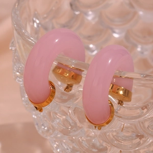 Detailed view of pink resin C-shaped hoop earrings on a decorative glass bowl
