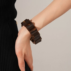 Close-up of a wide brown tortoiseshell resin bangle with textured wavy surface