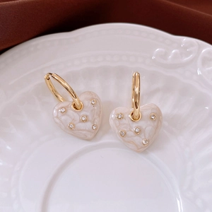 Detailed close-up of cream heart pendant earrings with sparkling crystals in a vintage dish