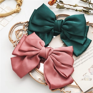 Detail of satin bow hair clips in emerald and pink showing silk texture on a gold tray