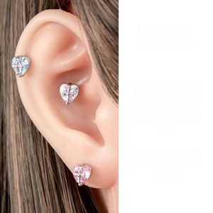 Detailed close-up of heart-shaped titanium steel ear studs with cross motif and gems
