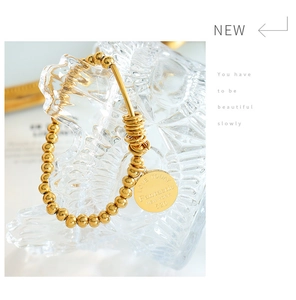 Detail of 18K gold-plated beaded bracelet featuring engraved round pendant and steel charms