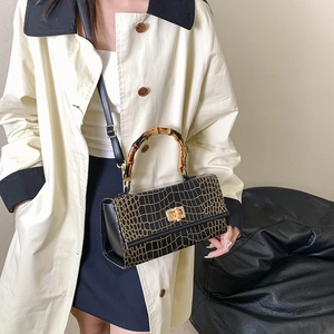 Detail showing bamboo handle and black crocodile pattern texture on a stylish handbag
