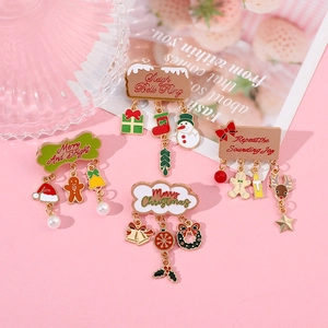 Close-up of colorful Christmas enamel brooches with dangling holiday charms on pink background