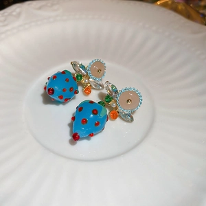 Detailed macro view of blue strawberry earrings with gold leaves and sparkling crystals