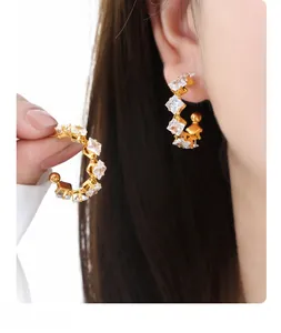 Detailed close-up of C-shaped 18K gold plated earrings with square claw-set zircon stones
