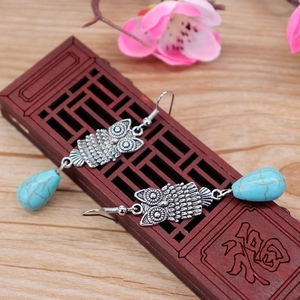 Detailed shot of retro owl earrings with silver feathers and turquoise waterdrop pendants