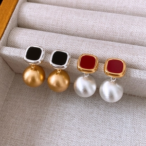 Detail view of retro square enamel earrings with metallic spheres on beige texture