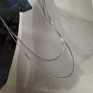 Detailed close-up of layered silver snake and box chain necklaces on a magazine