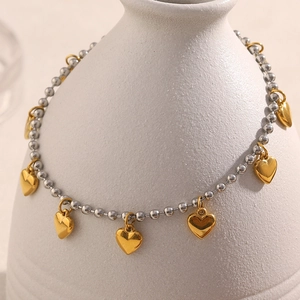 Detail view of 18K gold plated heart pendants and silver bead chain on a ceramic vase