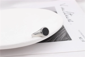 Macro detail of silver signet ring with black circular inlay on a white ceramic plate